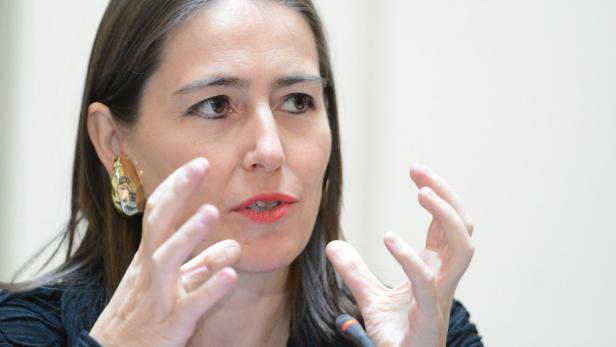 Eine Frau mit dunklen Haaren gestikuliert vor einem Mikrofon.