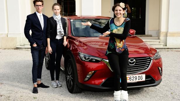 Drei junge Leute posieren vor einem roten Mazda CX-3.