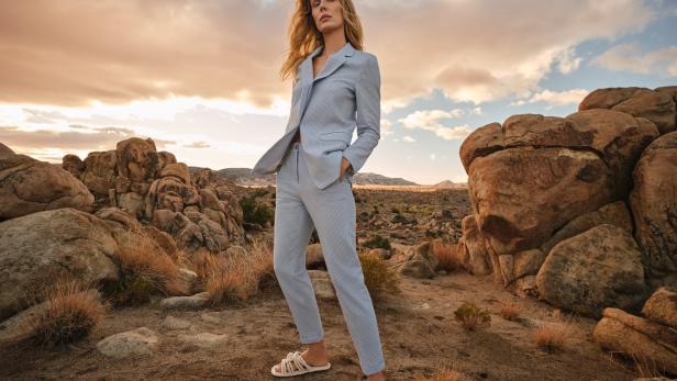 Eine Frau in einem hellblauen Anzug posiert in einer Wüstenlandschaft mit Felsen.