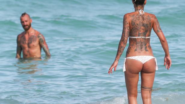 Meirelles Eine Frau mit Tätowierungen steht im Meer, ein Mann im Hintergrund.