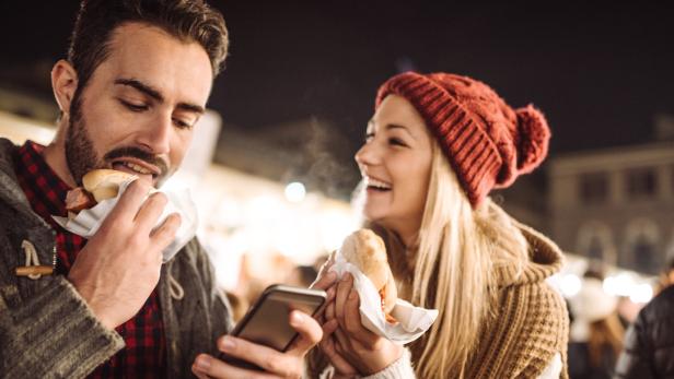 Ein Mann isst einen Hotdog, während eine Frau lacht und ebenfalls einen Hotdog hält.