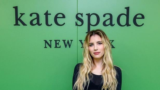 Emma Roberts posiert vor einem grünen „Kate Spade New York“-Hintergrund.