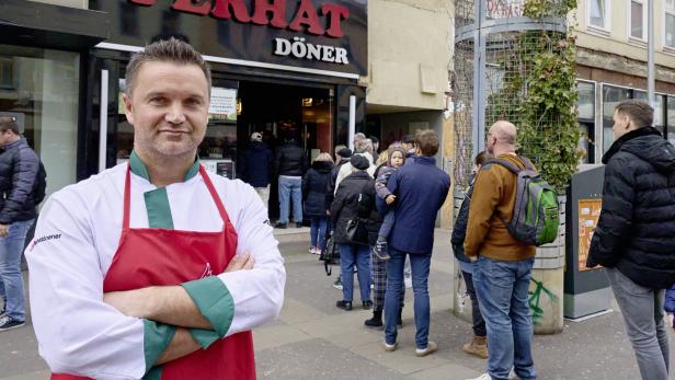 Ein Koch steht vor dem „Ferhat Döner“-Imbiss, vor dem eine Schlange wartet.