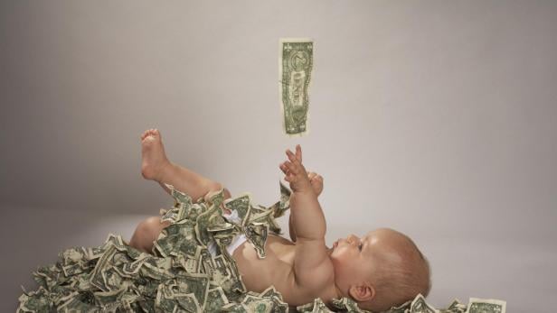 Ein Baby liegt auf dem Rücken, bedeckt mit US-Dollar-Scheinen, die von oben fallen.