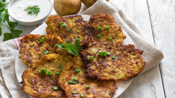 Ein Teller Kartoffelpuffer, garniert mit Schnittlauch und Petersilie, dazu ein Schälchen Sour Cream.