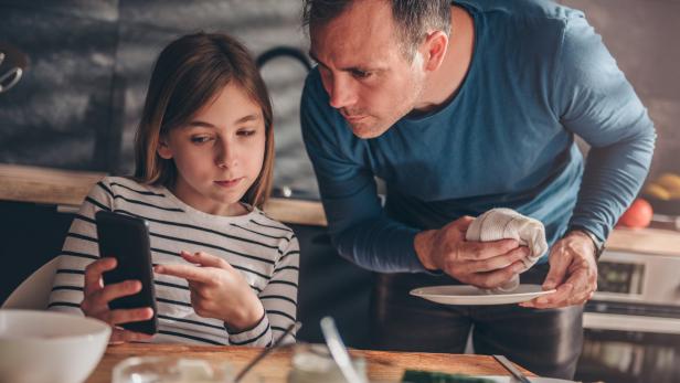 Eine Tochter zeigt ihrem Vater, was sie sich am Smartphone ansieht.