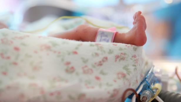 Ein Babyfuß mit Namensbändchen ragt aus einer Decke mit Blumenmuster.
