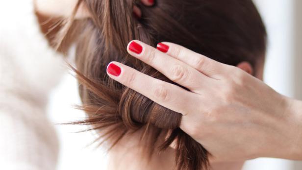 Eine Frau mit rotem Nagellack steckt ihr braunes Haar hoch.