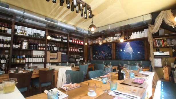 Innenansicht eines Restaurants mit gedeckten Holztischen und Weinregalen.