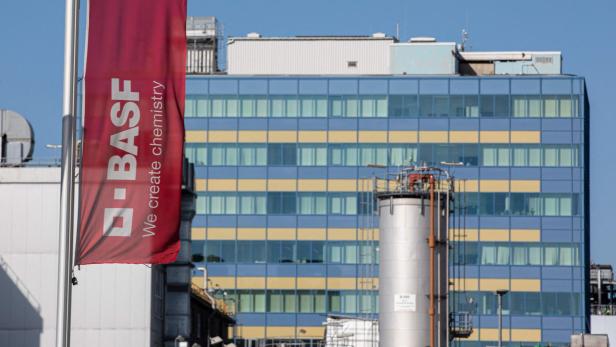 Eine BASF-Flagge weht vor einem Verwaltungsgebäude und Industrieanlagen.