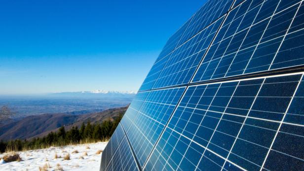 Solarzellen auf einem schneebedeckten Hügel mit Blick auf eine Berglandschaft.