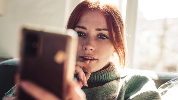 Woman with red hair looking on screen of her mobile phone. - Stock-Fotografie