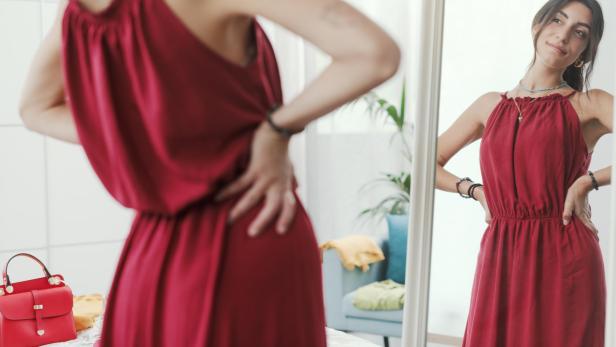 Eine Frau probiert ein rotes Kleid vor dem Spiegel an.