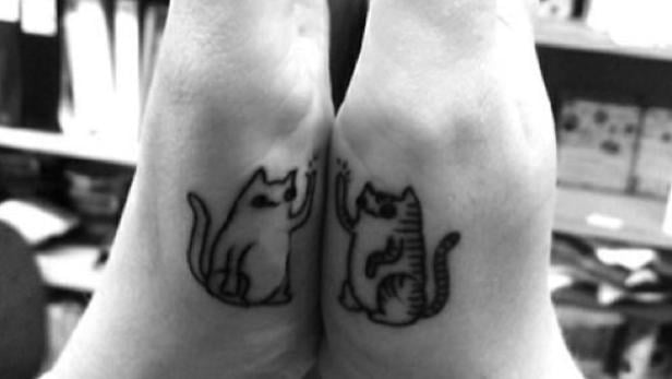 Zwei Handgelenke mit passenden Tattoo-Zeichnungen von Katzen, die sich zuwinken.