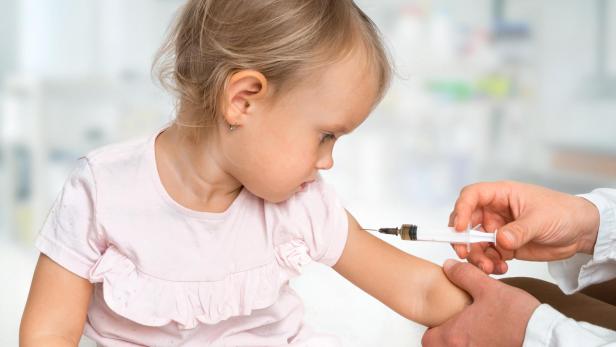 Pediatrician doctor is injecting vaccine to shoulder of baby