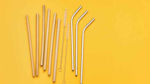 Mehrere wiederverwendbare Strohhalme aus Bambus und Edelstahl liegen auf einem gelben Hintergrund.