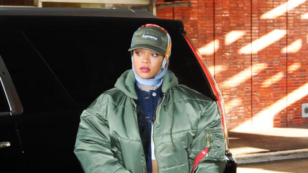 Rihanna verlässt ein Gebäude mit einer grünen Jacke, einer Supreme-Kappe und einer Dior-Tasche.