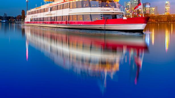 Ein Ausflugsschiff auf der Donau in Wien vor der Skyline der Stadt.