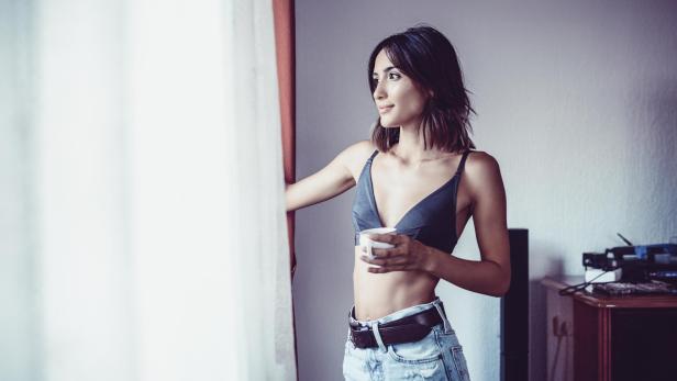 Eine Frau trinkt Kaffee und blickt aus dem Wohnzimmerfenster.