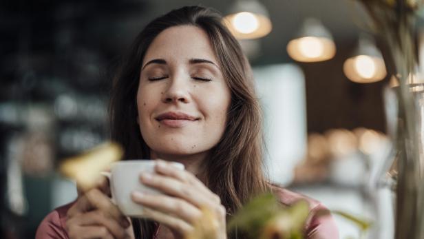 Eine lächelnde Geschäftsfrau riecht an ihrem Kaffee in einem Café.