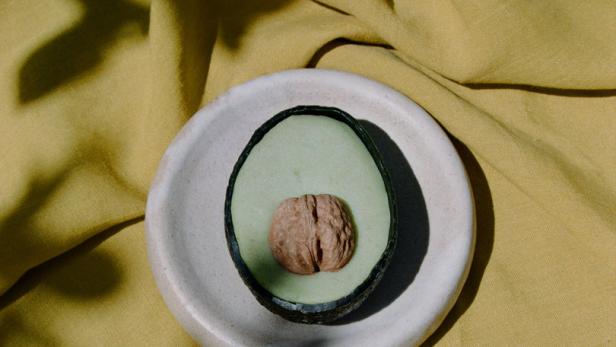 Eine halbe Avocado liegt auf einem Teller, der auf einem gelben Tuch platziert ist.