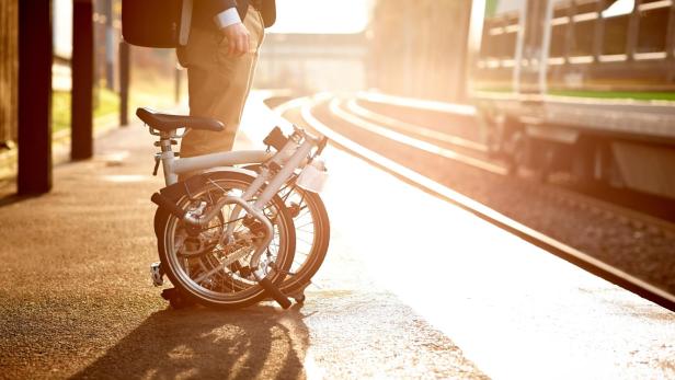Ein Geschäftsmann wartet mit einem Faltrad auf dem Bahnsteig.