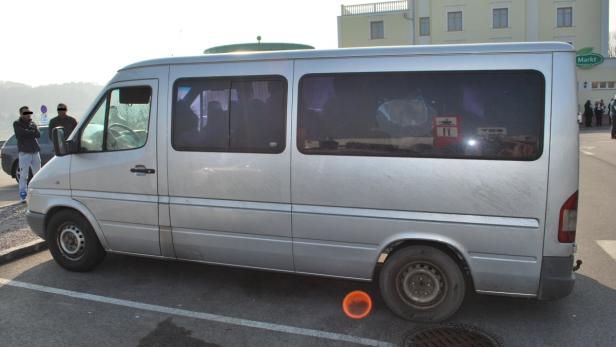 Ein silberner Transporter steht auf einem Parkplatz vor einem Gebäude mit der Aufschrift „Markt“.