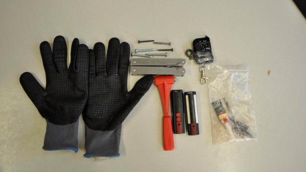 Ein Paar Arbeitshandschuhe, Schrauben, Multitools, ein Nothammer und ein Garagentoröffner liegen auf einem Tisch.
