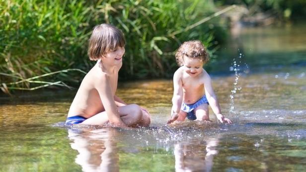 Zwei Kinder spielen im seichten Wasser eines Flusses.