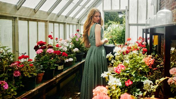Eine Frau in einem grünen Kleid gießt in einem Gewächshaus Blumen.
