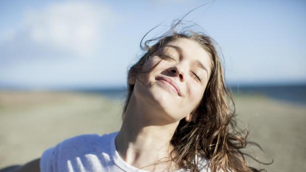 Junge Frau mit geschlossenen Augen lächelt an einem Strand.