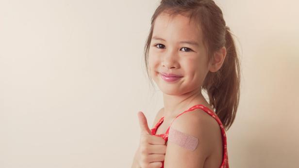 Happy mixed Asian girl giving thumb up and showing her arm with bandage after got vaccinated or inoculation USA: Ein Viertel der Eltern verschwieg Corona-Infektion der Kinder