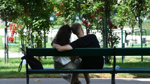 Ein Paar sitzt auf einer Parkbank, umgeben von Rosenbüschen.