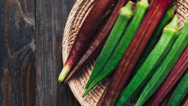 Grüne und rote Okraschoten liegen in einem geflochtenen Korb.