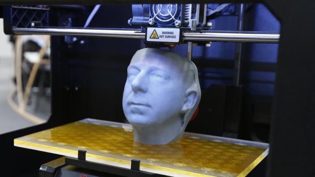 Ein 3D-Drucker druckt ein graues Modell eines menschlichen Kopfes.
