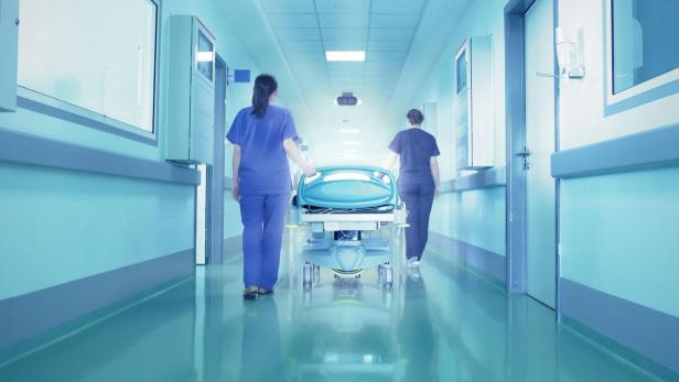 Zwei Krankenschwestern schieben eine leere Trage durch einen Krankenhausflur.