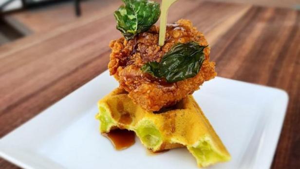 Ein Teller mit Hähnchen und Waffeln, garniert mit Basilikumblättern.