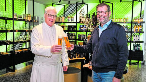 Zwei Männer stoßen in einem Geschäft mit Gläsern der Biermarke Schlägl an.