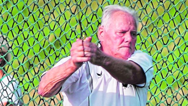 Ein älterer Mann im Sportdress hält einen Hammerwurfhammer fest umklammert.