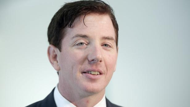 Ein Porträt eines Mannes in einem dunklen Anzug vor einem hellen Hintergrund.