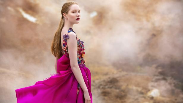Eine Frau in einem pinkfarbenen Kleid mit Blumenapplikationen blickt über ihre Schulter.