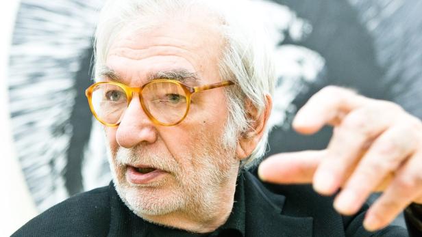 Ein Mann mit Brille gestikuliert vor einem unscharfen Hintergrund.