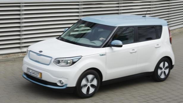 Ein weißer Kia Soul EV mit blauem Dach steht vor einer Wand.