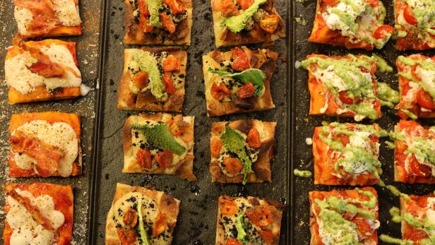 Verschiedene Pizzastücke mit unterschiedlichen Belägen auf einem schwarzen Blech.