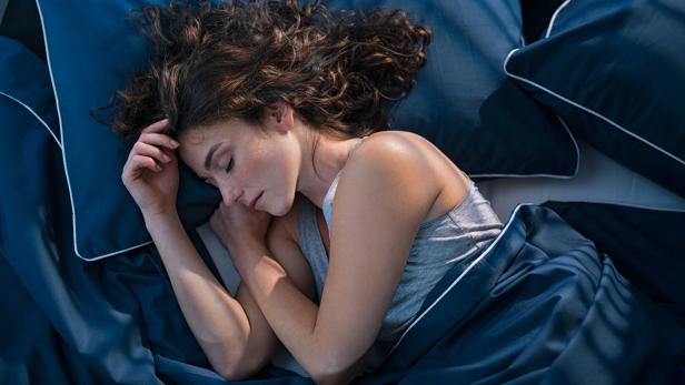 Junge Frau schläft mit Leintuch im Bett. 