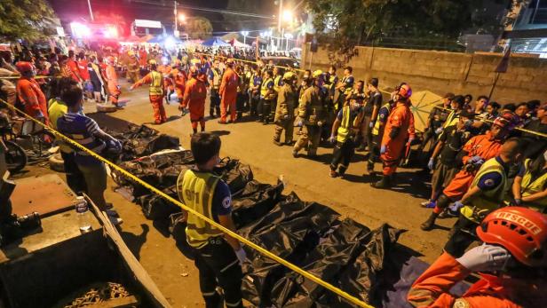Rettungskräfte stehen neben Leichensäcken, die mit gelbem Absperrband umgeben sind.