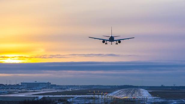 Ein Flugzeug landet auf der Landebahn eines Flughafens bei Sonnenuntergang.
