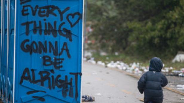 Ein kleines Kind läuft an einer blauen Toilette mit der Aufschrift „Everything gonna be alright“ vorbei.