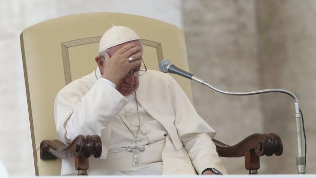 Papst Franziskus sitzt mit gesenktem Kopf und Hand vor dem Gesicht an einem Tisch mit Mikrofon.