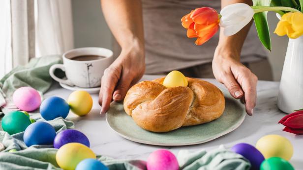 Ein Osterbrot mit einem gelben Ei wird von bunten Ostereiern und Tulpen umgeben.